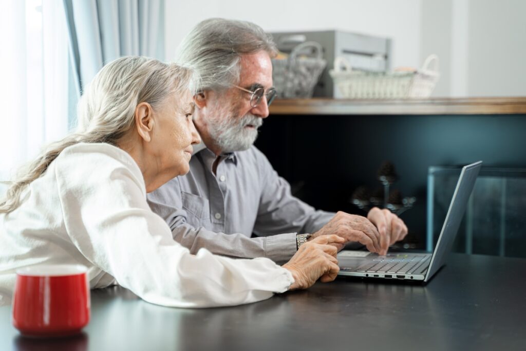 Happy family spouses sitting looking at computer screen at living room,Smiling middle aged man showing video on laptop,Retirement weekend lifestyle concept.