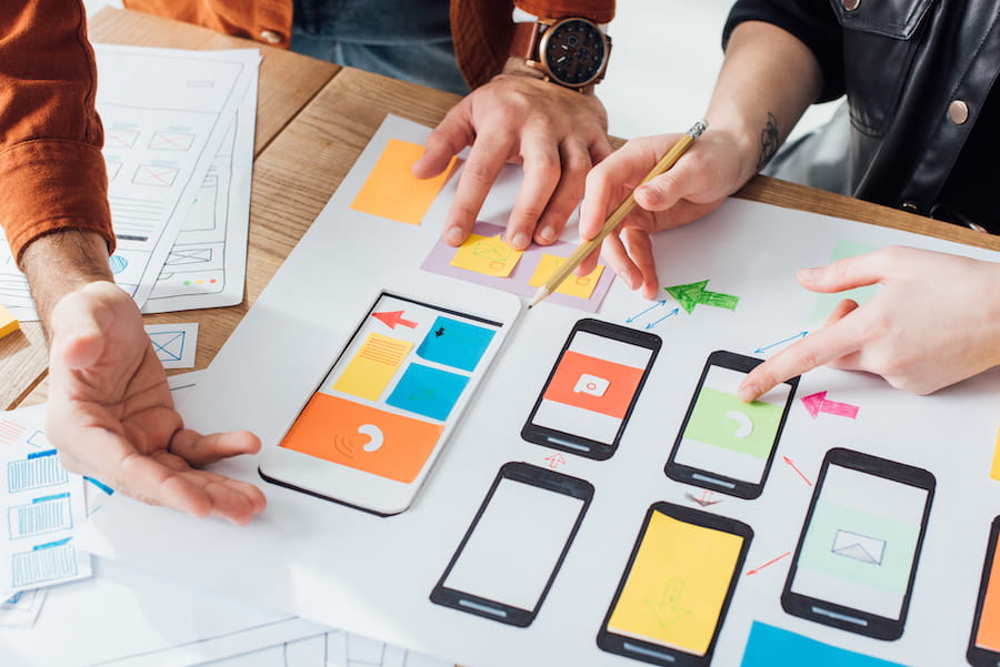 Cropped view of developers creative user experience design of mobile website with layouts on table
